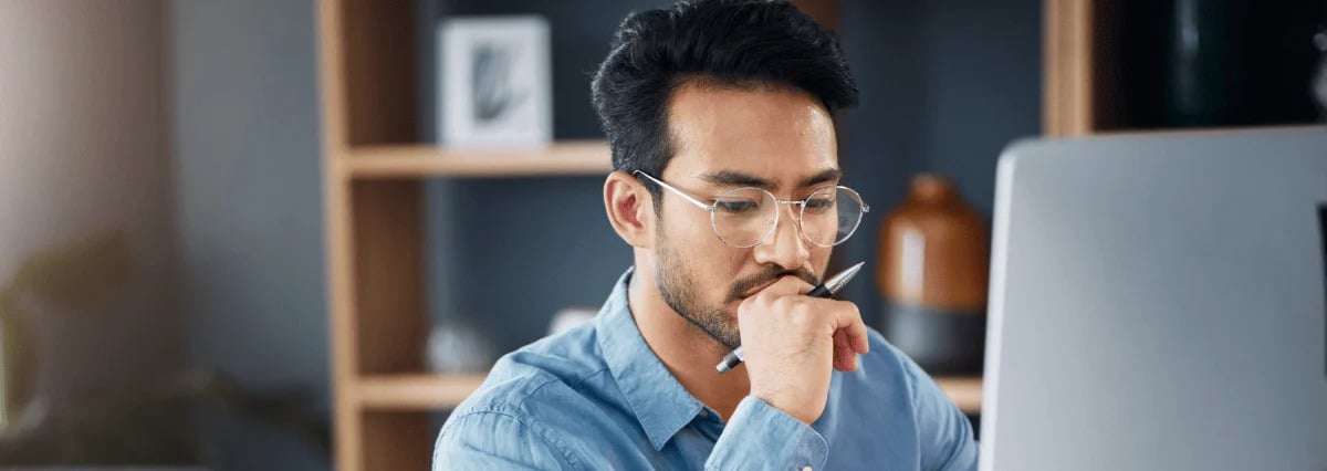 Un homme en face d'un ordinateur qui tient un stylo dans sa main